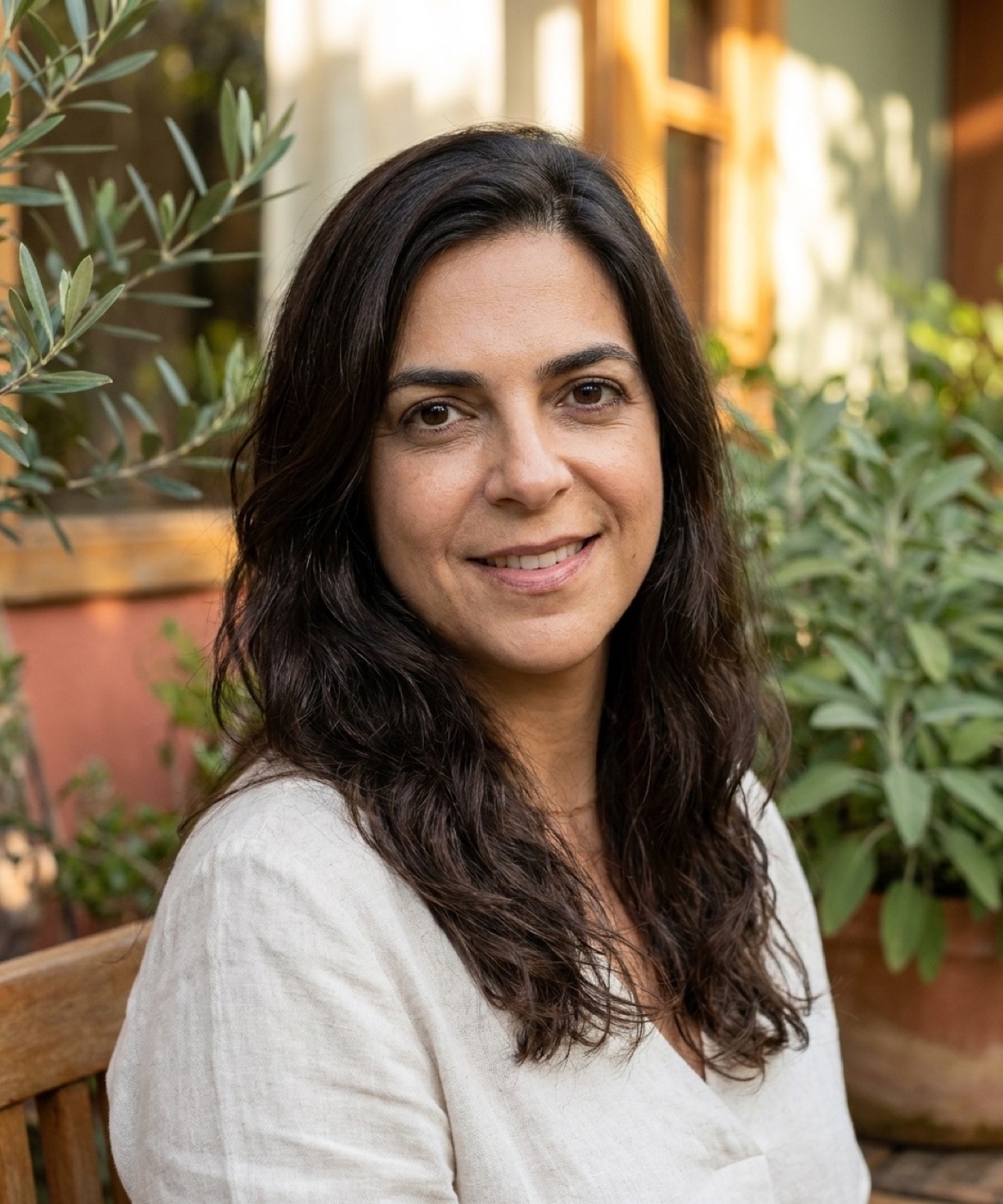 Retrato de Márcia Regina, terapeuta integrativa, sorrindo no jardim entre oliveira e sálvia